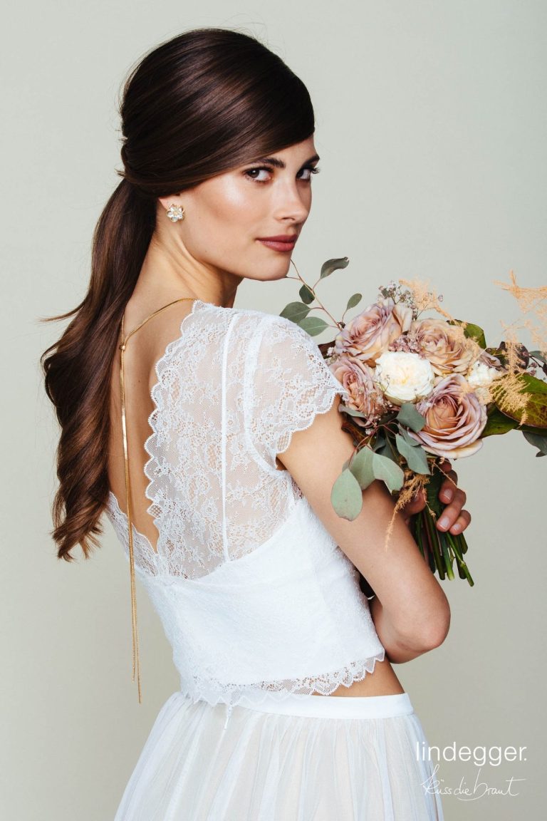 Zweiteiler: Frau in eleganter, weißer Bluse und heller, grünfarbener Midi-Rock steht vor klassischer Architektur.